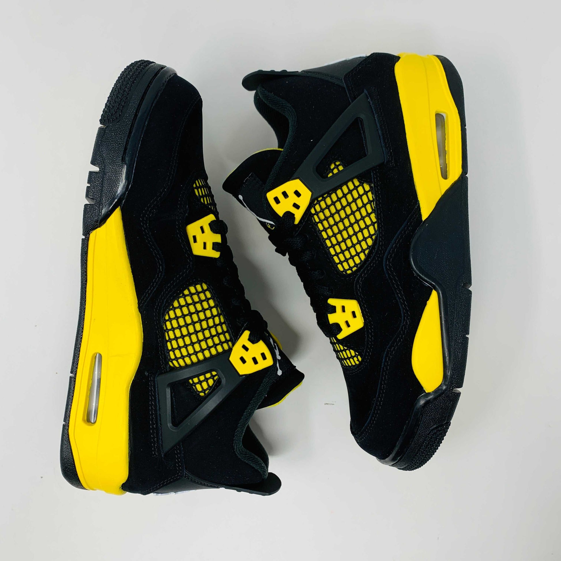Brand new for 2023, the Jordan 4 Retro Thunder (GS) sneakers in black and yellow feature mesh panels and air cushioning. Positioned on a white background, they showcase their unique color scheme and design.