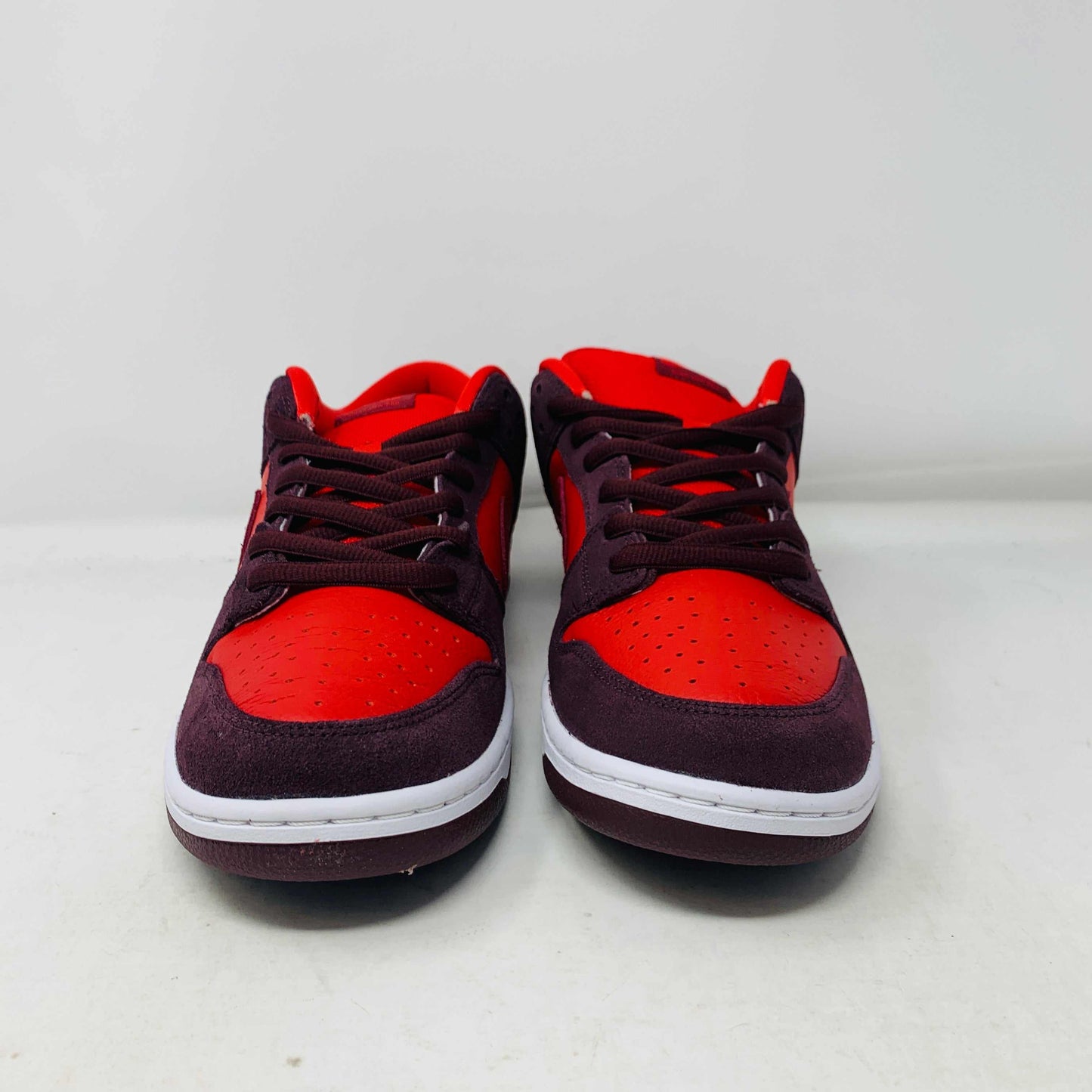 A 100% authentic, brand new Nike SB Dunk Low Cherry sneaker in red and dark brown sits on a branded purple Nike SB shoebox. It features a red swoosh, toe box, dark brown overlays, extra laces, white midsole, and dark brown outsole.