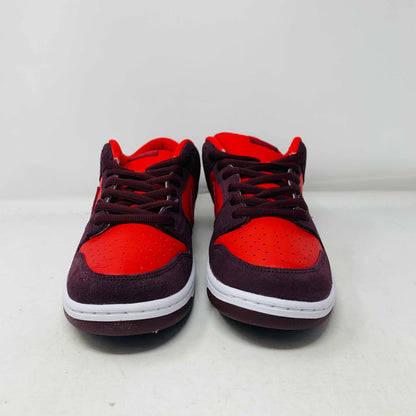 A 100% authentic, brand new Nike SB Dunk Low Cherry sneaker in red and dark brown sits on a branded purple Nike SB shoebox. It features a red swoosh, toe box, dark brown overlays, extra laces, white midsole, and dark brown outsole.