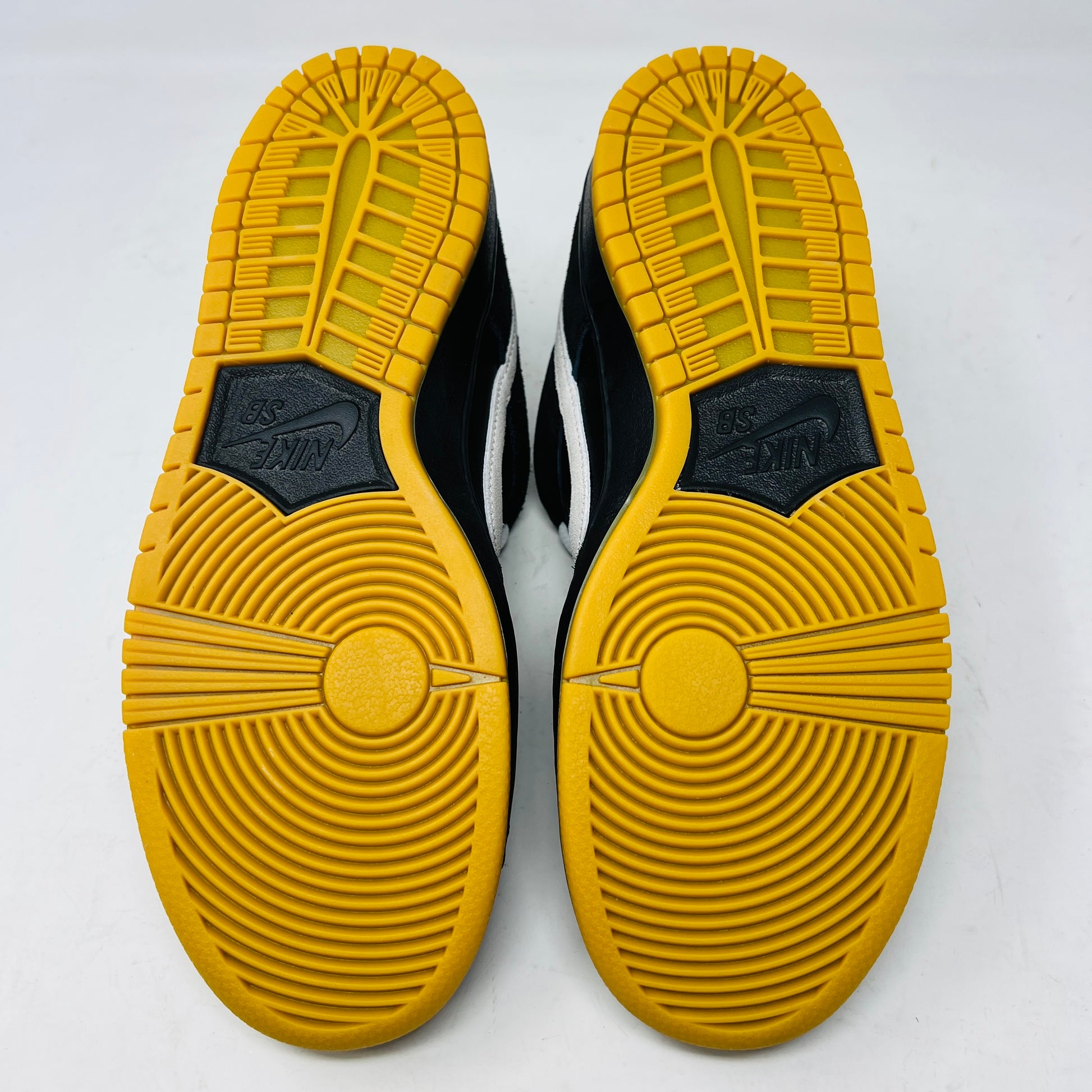 A black Nike Dunk Low Pro SB Black White Gum sneaker with white laces and swoosh sits on a purple Nike SB box. The 2025 shoe has a yellow sole, leather-texture finish, and both are in new condition.