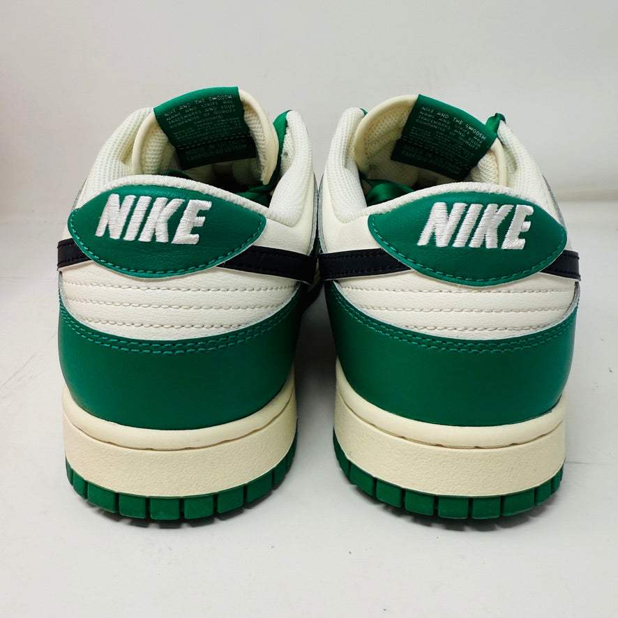 The Nike Dunk Low SE Lottery Pack Malachite Green sneaker, from the 2022 collection, is displayed on a red Nike shoebox. It features clean green and white uppers, a black swoosh logo, and a white midsole. The partially open lid shows essential shoe information and size labels.