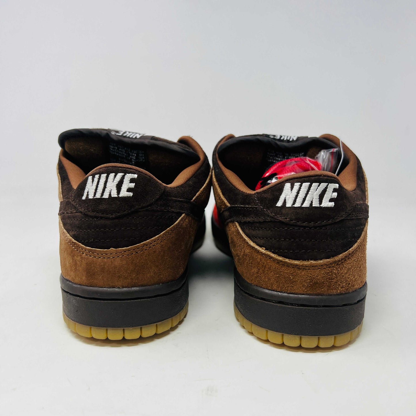 A pair of BRAND NEW Nike SB Dunk Low Bison sneakers featuring brown and red suede uppers, black laces, EXTRA LACES included, and a light brown sole. Positioned side by side on a white background, they promise to be 100% authentic and stylish.