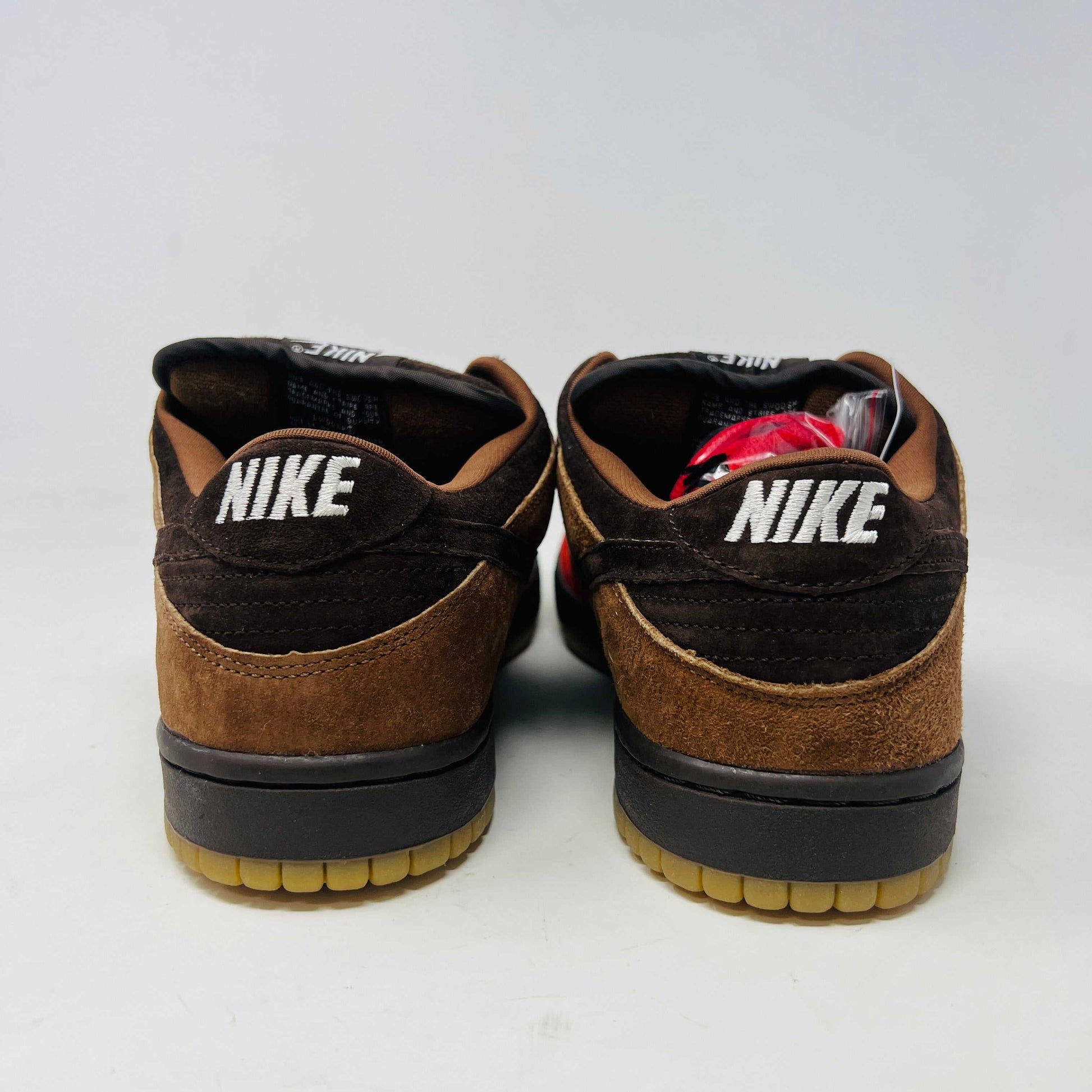 A pair of BRAND NEW Nike SB Dunk Low Bison sneakers featuring brown and red suede uppers, black laces, EXTRA LACES included, and a light brown sole. Positioned side by side on a white background, they promise to be 100% authentic and stylish.