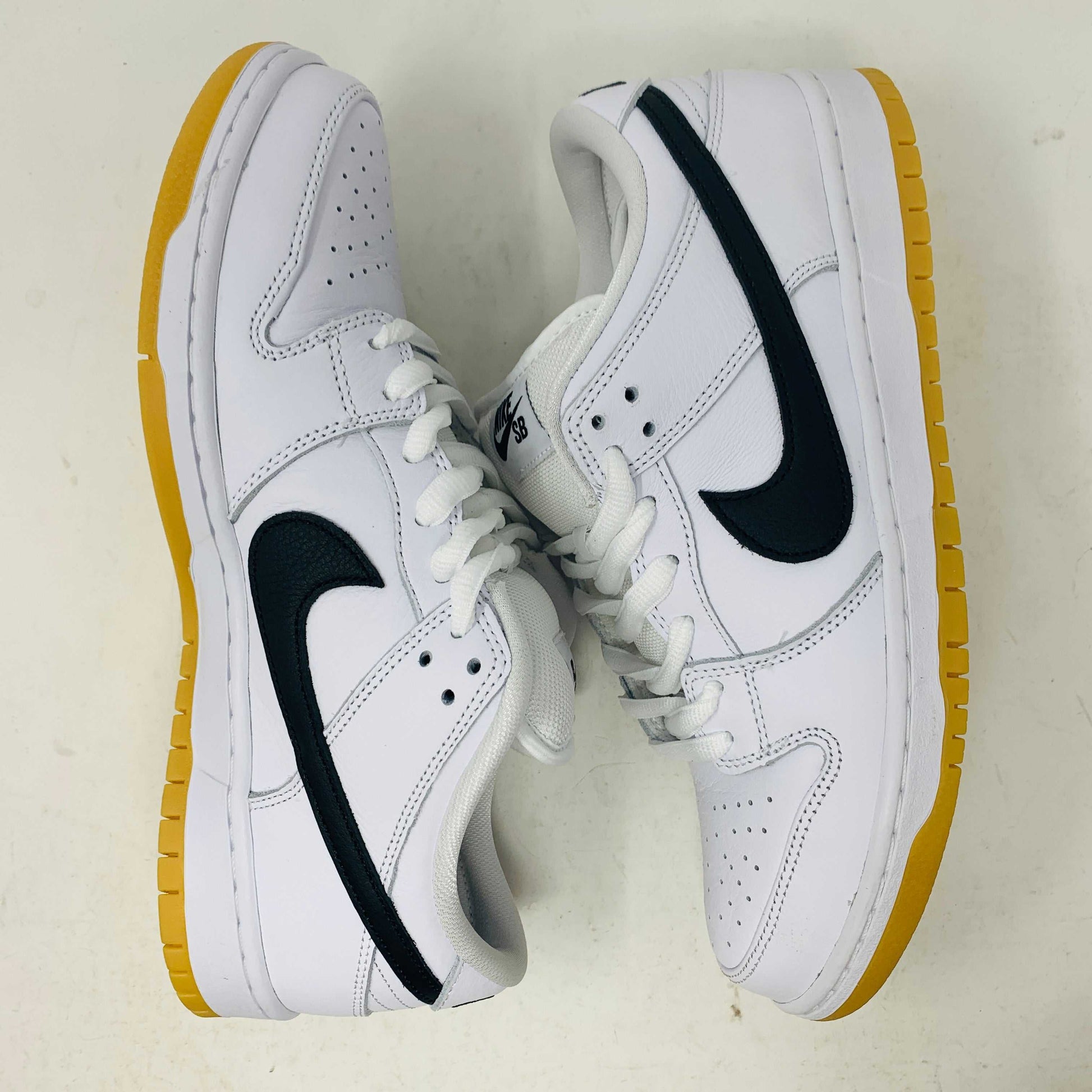 A brand new Nike SB Dunk Low in white with a black swoosh, white laces, and a gum sole rests on a 2023 purple Nike SB shoebox featuring bold white text. The profile view showcases its authentic design.