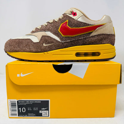 Nike Air Max 1 sneaker with brown suede, red and yellow swoosh, displayed on yellow Nike box