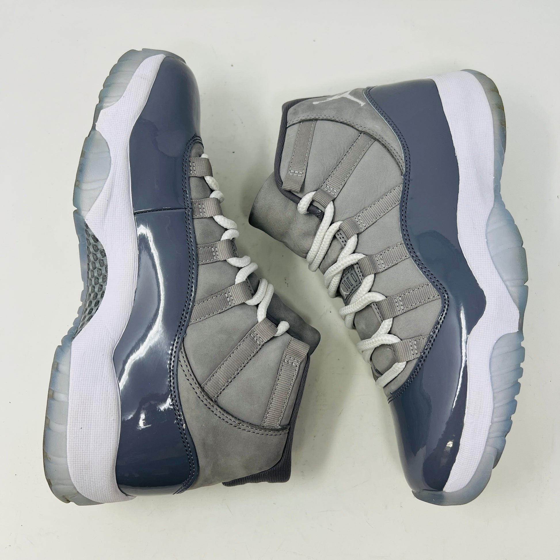 The Jordan 11 Retro Cool Grey (2021) sneaker, featuring clean gray and white uppers with glossy patent leather accents and white laces, is displayed on a gray Nike Air shoebox. The shoe is authentic in size 9.5, with the box in good condition.